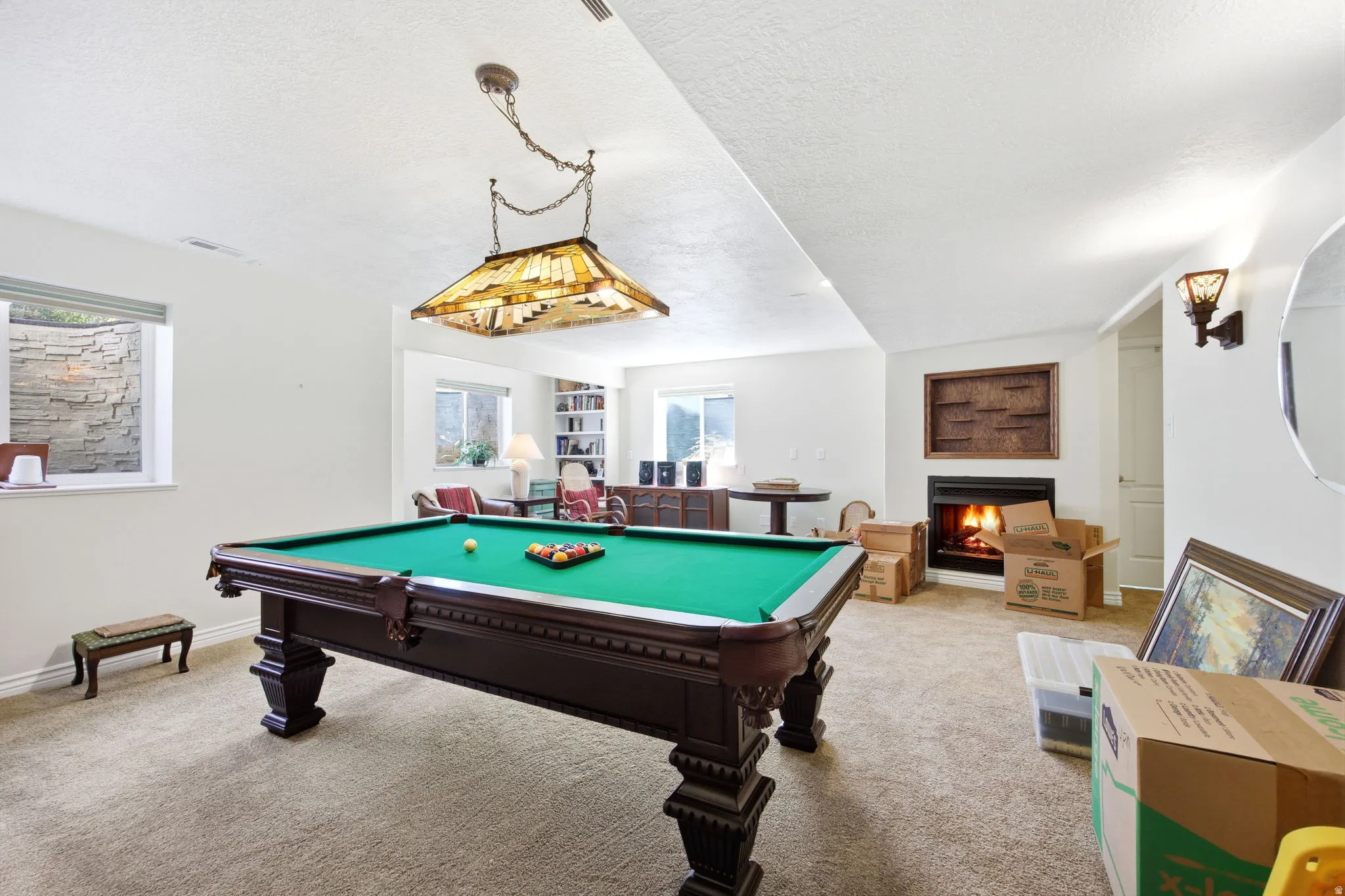 Spacious recreation room featuring a billiards table with an overhead Tiffany-style light fixture, a built-in fireplace, and recessed windows