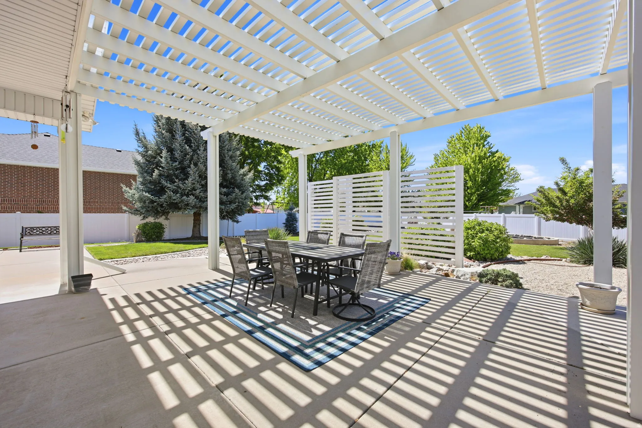 Spacious concrete patio featuring a white slatted pergola, providing shade and outdoor living space