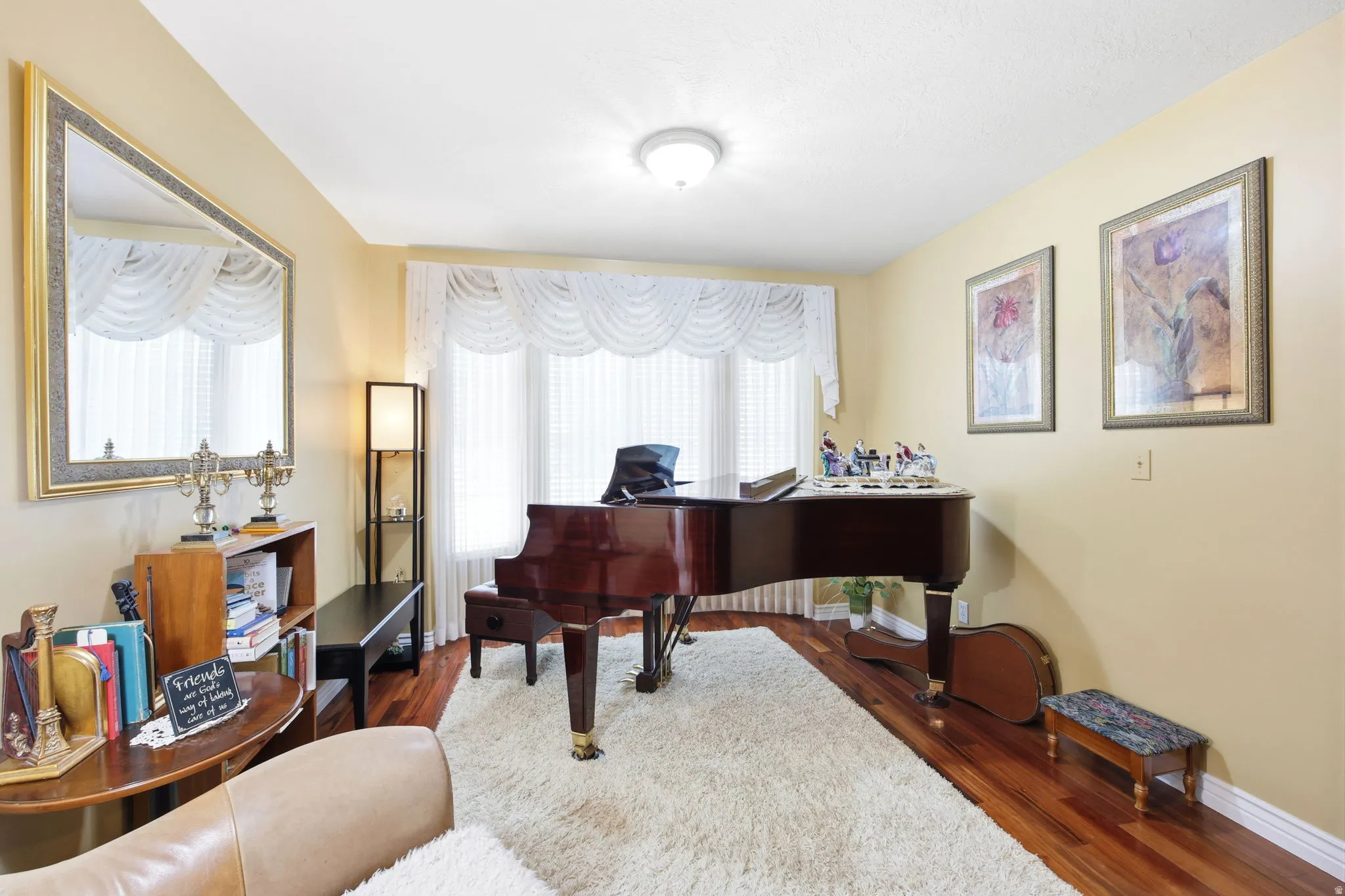 Living space featuring wood-finish flooring, a large bay window with white valances, and light-toned wall paint