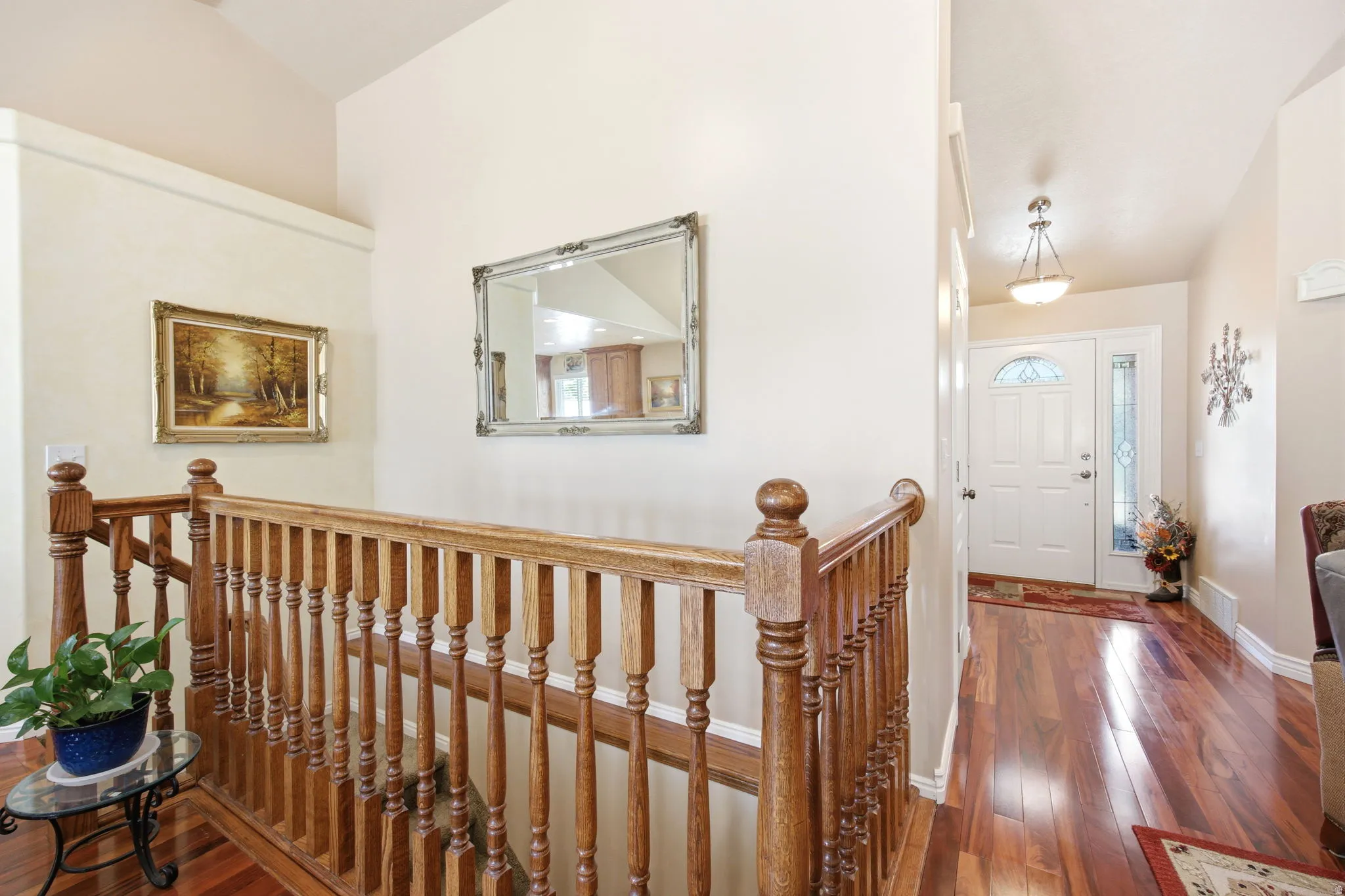 Hardwood flooring throughout the entry, spindle staircase with wood newel post, and vaulted ceiling