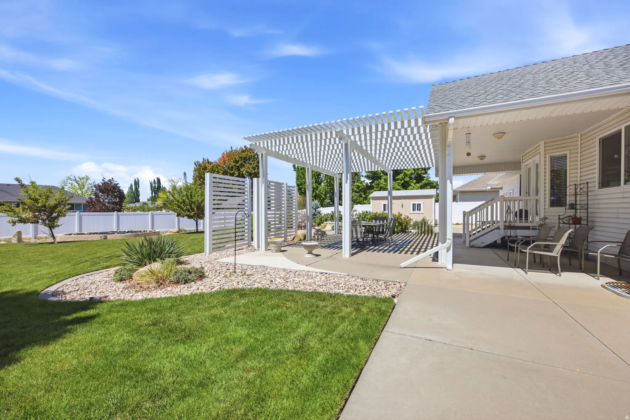 Expansive backyard with a manicured lawn, a large concrete patio, and a white slatted pergola