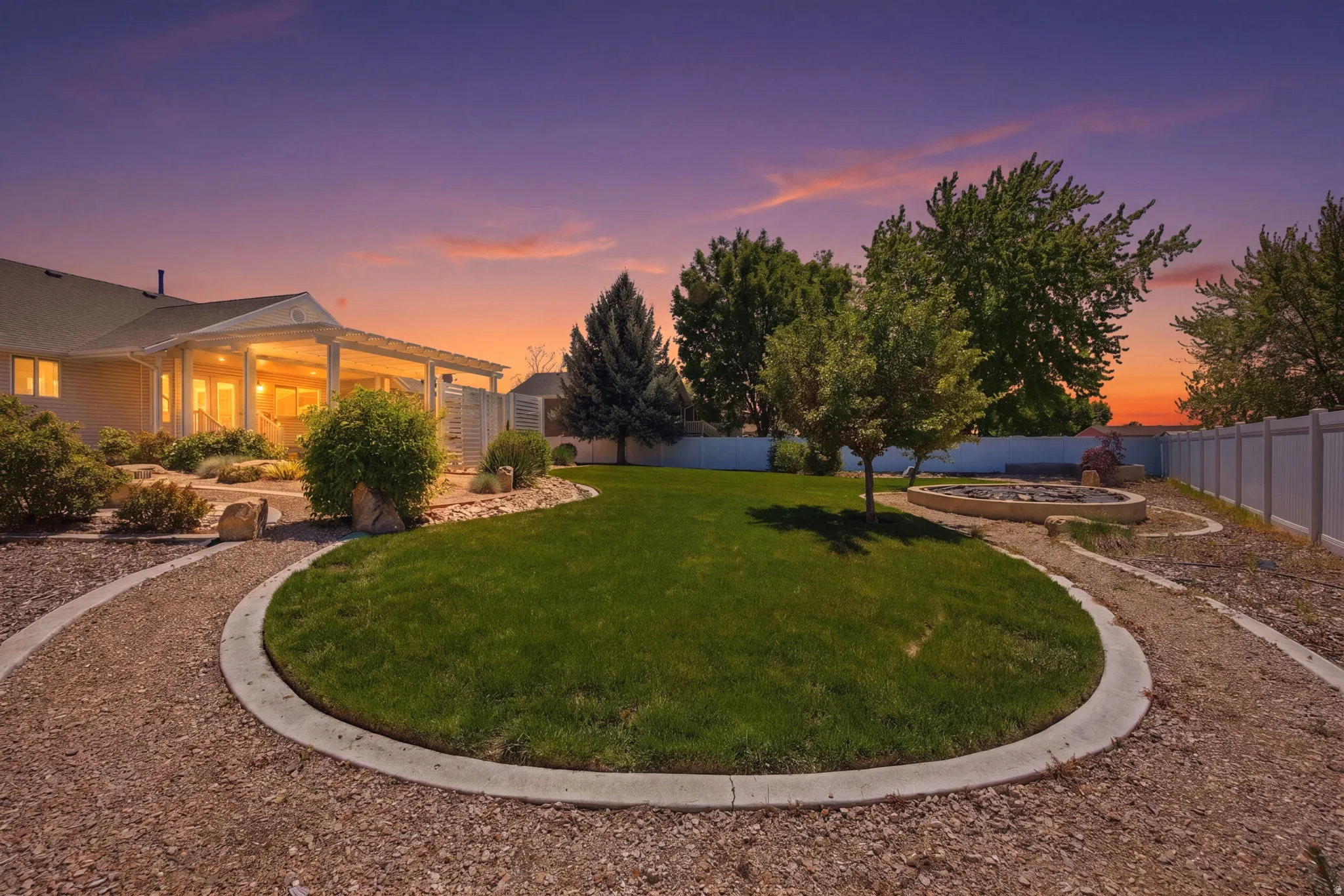 Landscaped backyard featuring a circular lawn area, gravel pathways, and a built-in fire pit