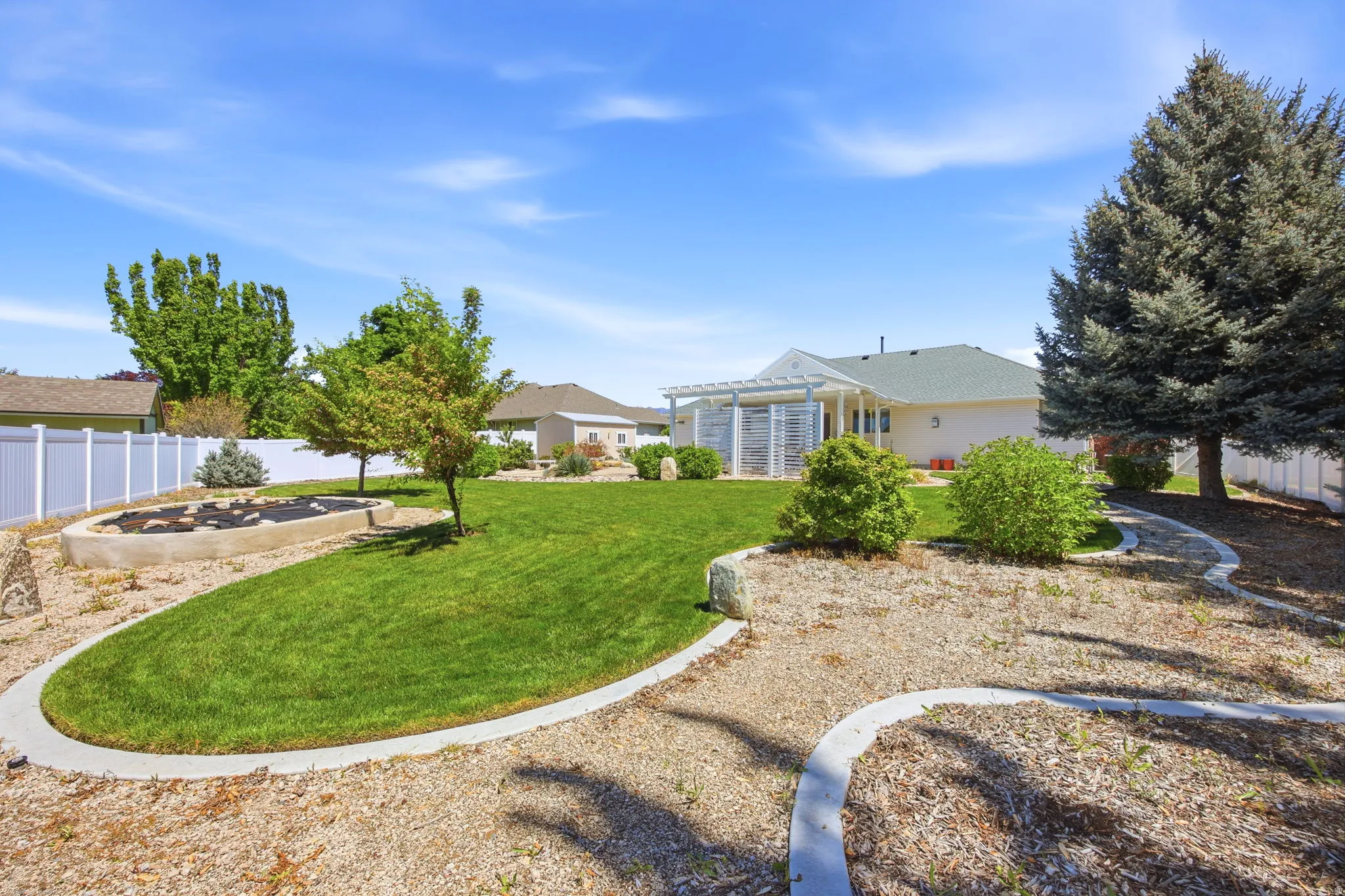 Landscaped backyard featuring a manicured lawn, established trees, and a white pergola structure