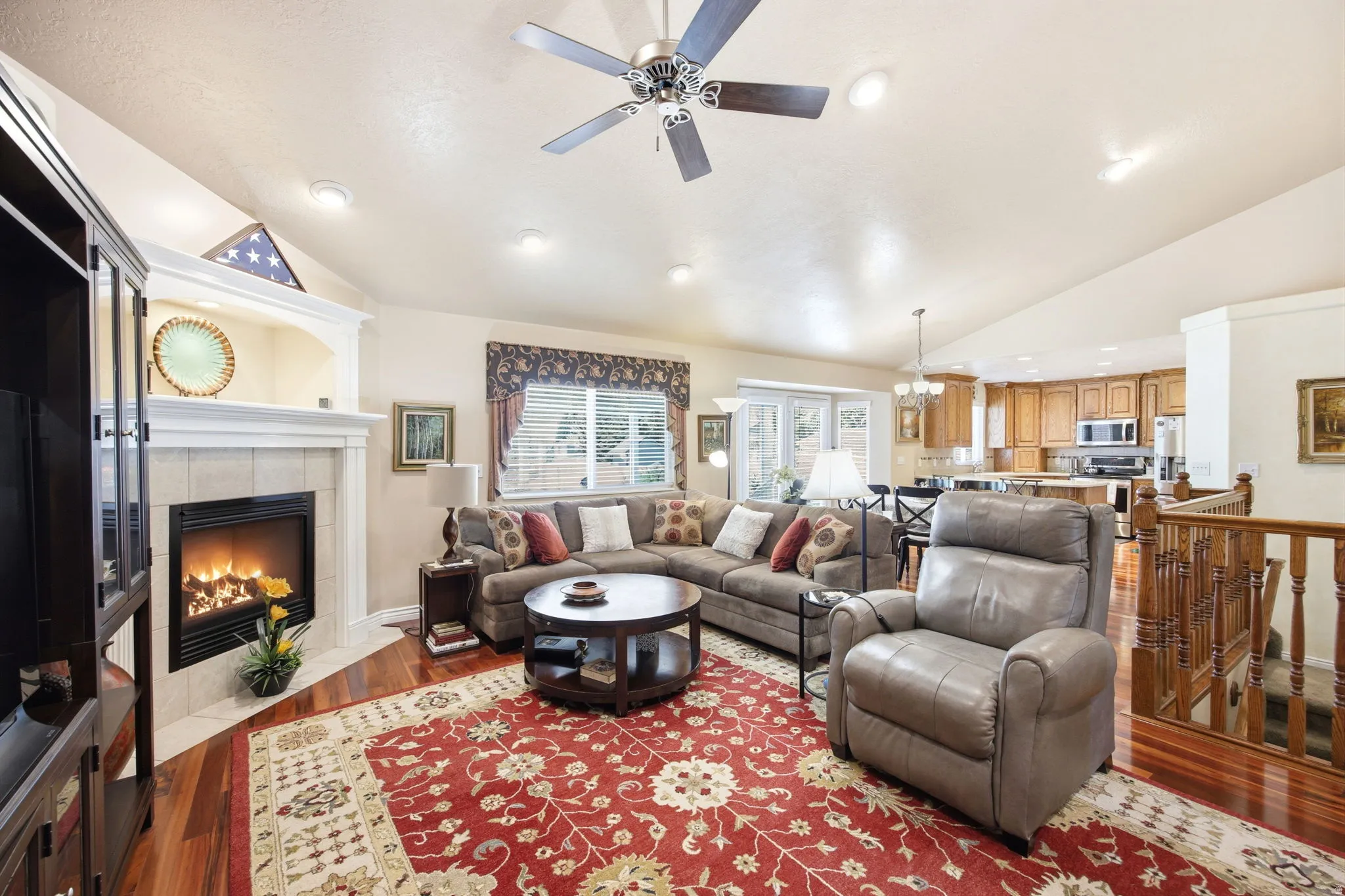 Living area featuring wood-finish flooring, a fireplace with tile surround and white mantel, and vaulted ceilings with recessed lighting