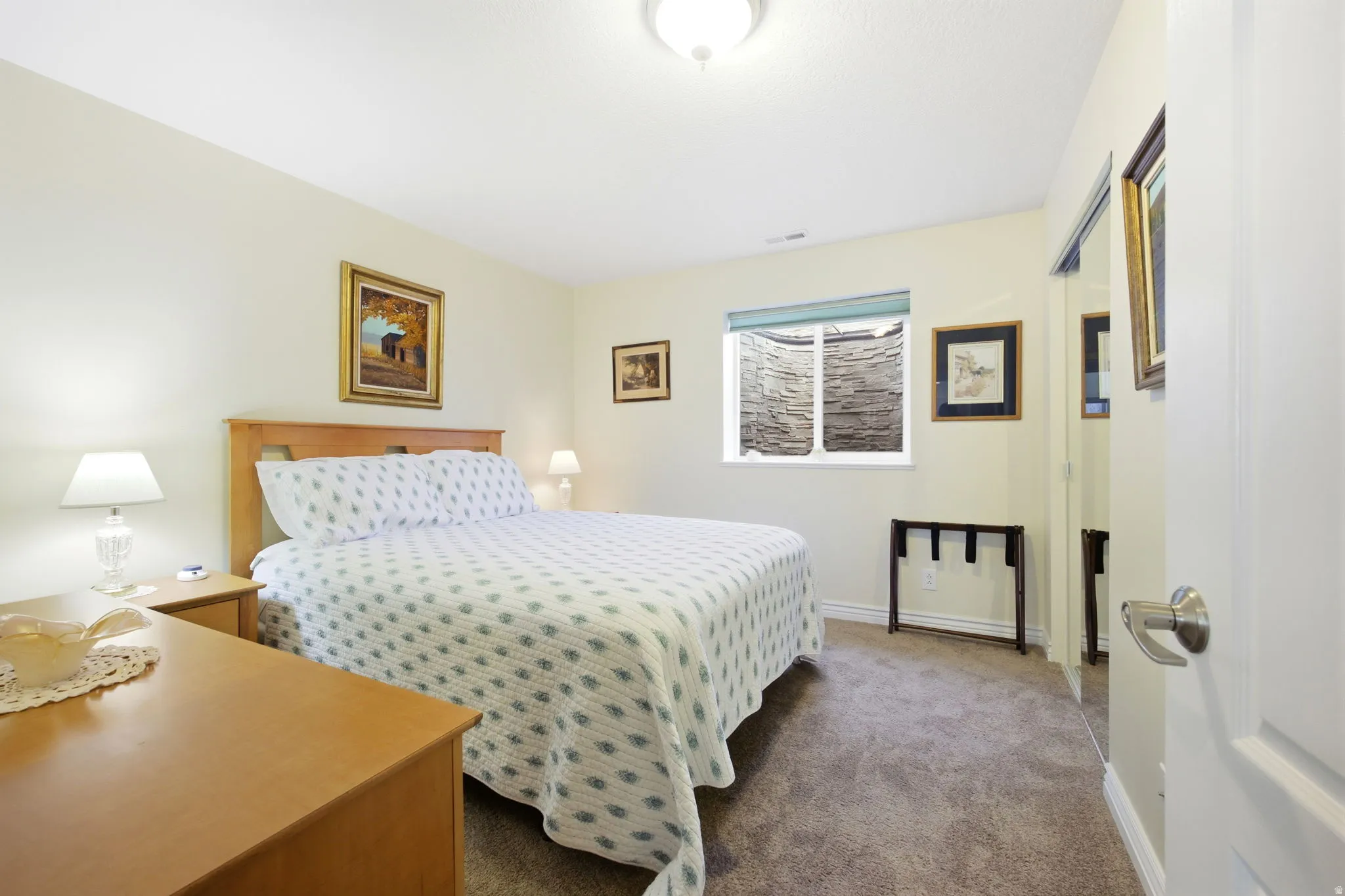 Bedroom featuring a window with a stone-lined window well, light cream walls, and a light wood-finish headboard