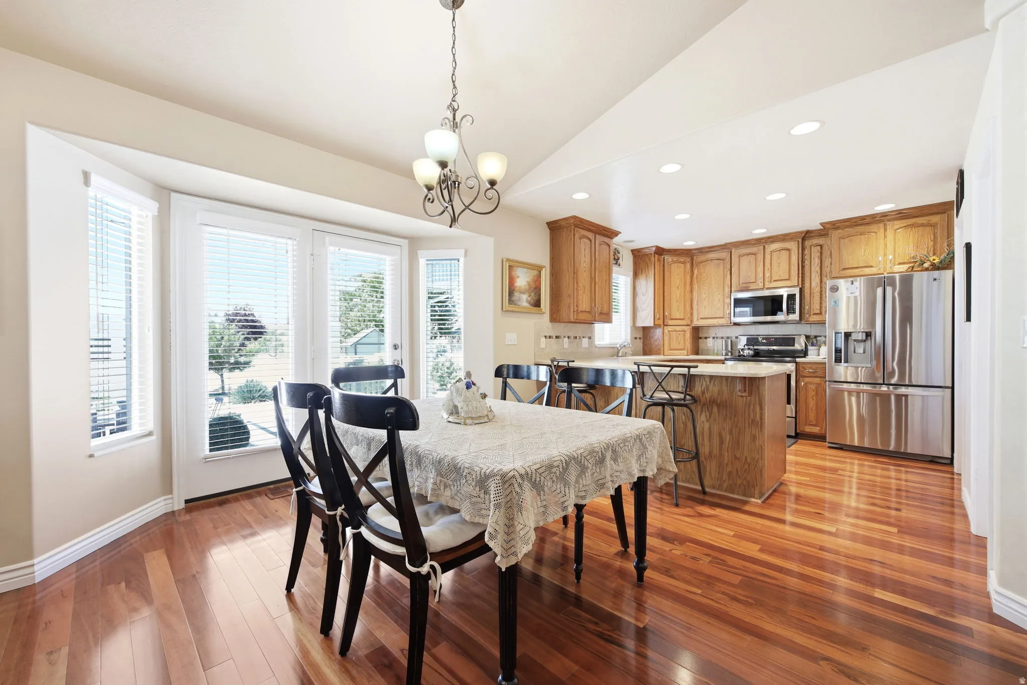 Open-concept living space featuring wood-finish flooring, a kitchen island with seating, stainless steel appliances, and a bay window