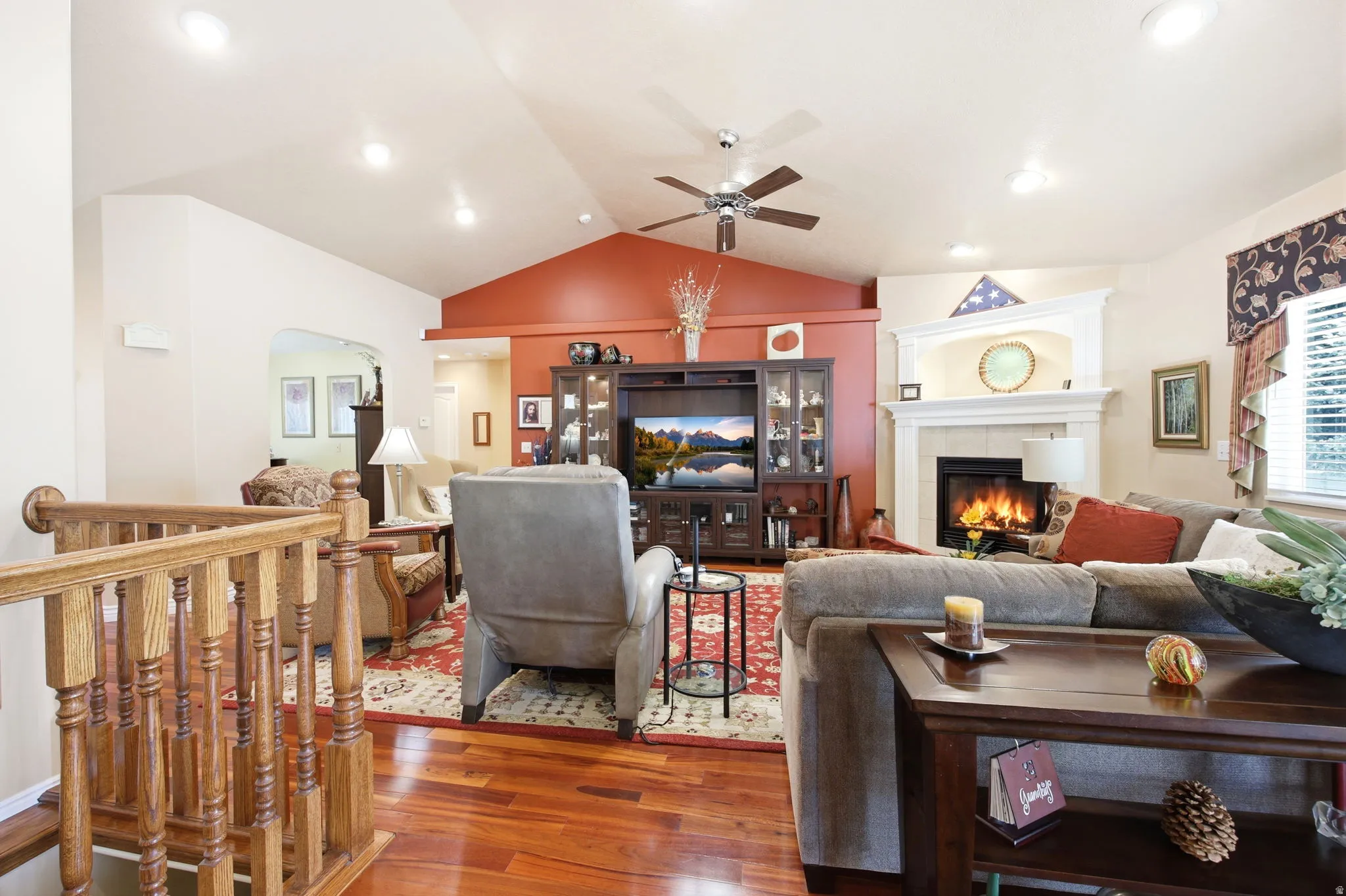 Living area featuring vaulted ceilings, wood-finish flooring, a fireplace with a white mantel, recessed lighting, and a ceiling fan
