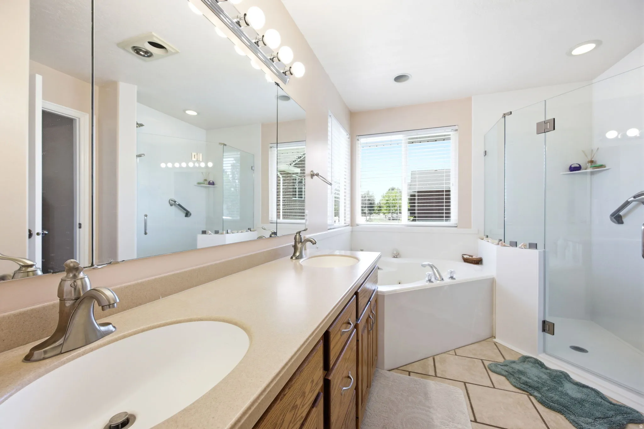 Double vanity with undermount sinks, a built-in corner soaking tub, a separate glass-enclosed shower, and a large wall mirror