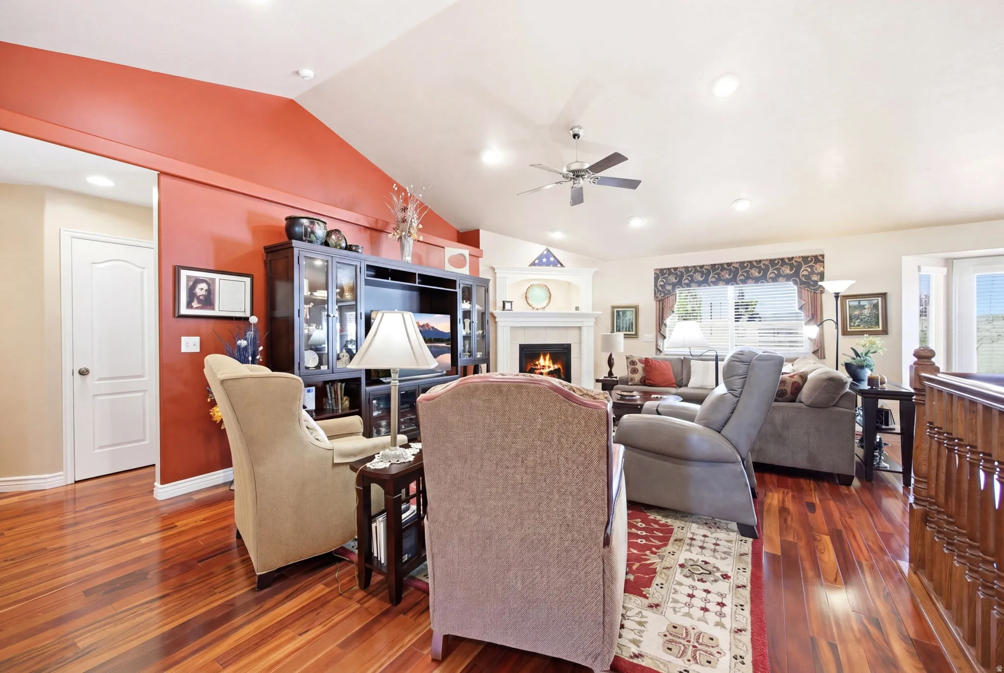 Spacious living area featuring rich wood-finish flooring, a contemporary ceiling fan, recessed lighting, a built-in entertainment center, and a fireplace with a white mantel