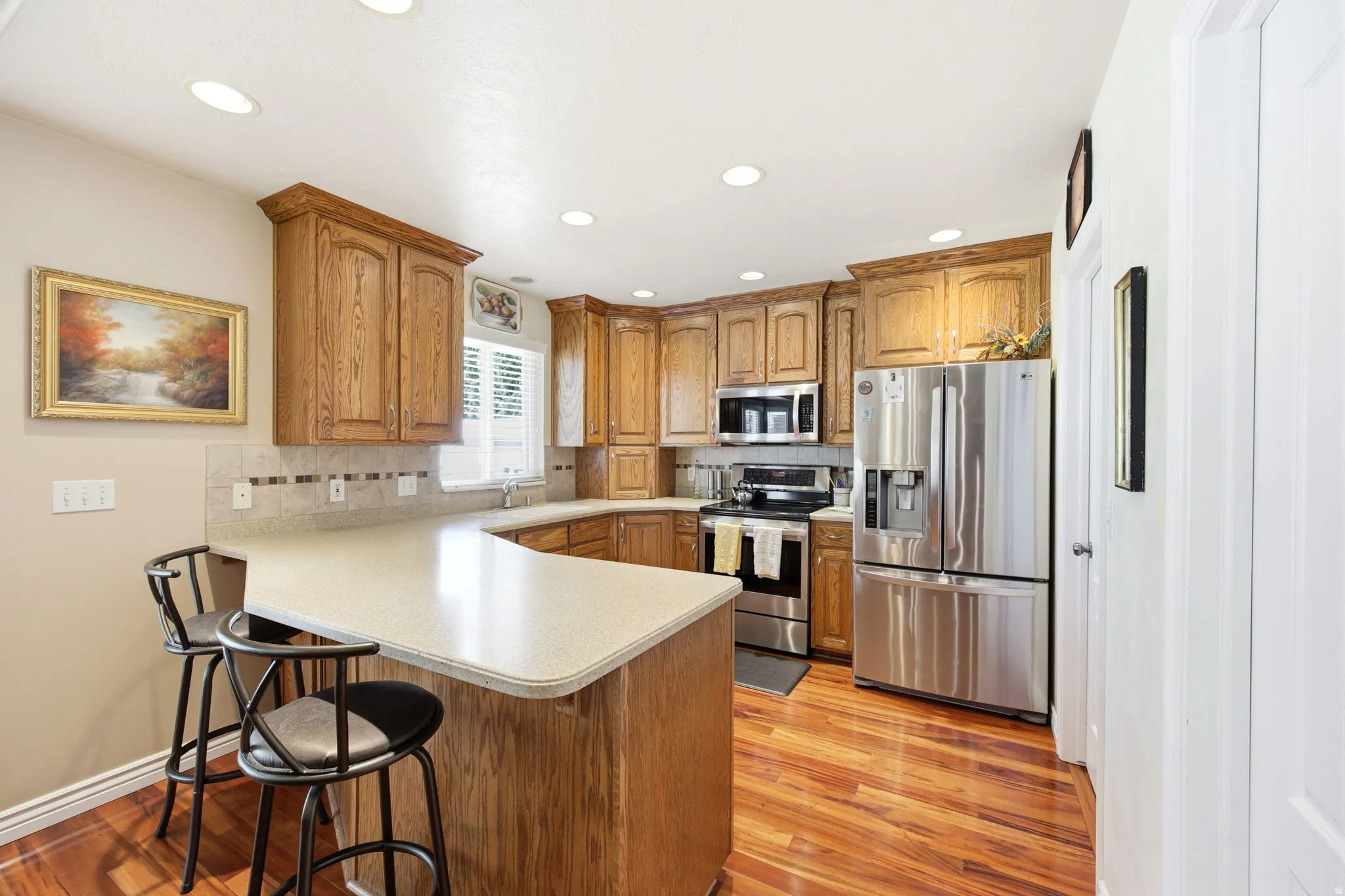 Kitchen featuring wood cabinetry, stainless steel appliances, a light-toned countertop, tile backsplash, and wood-finish flooring