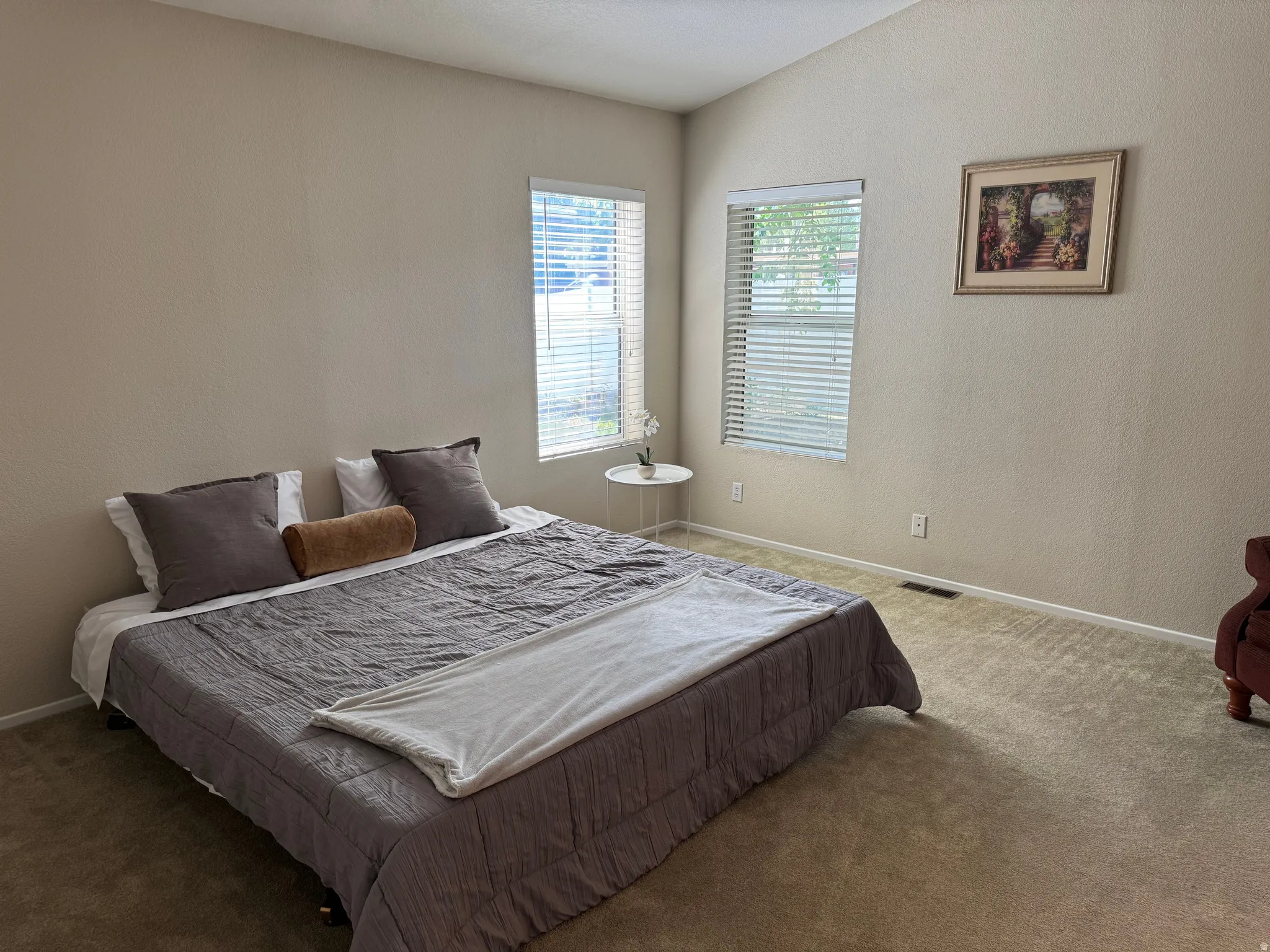 Vaulted ceiling room featuring two windows with horizontal blinds and neutral-toned wall-to-wall carpeting