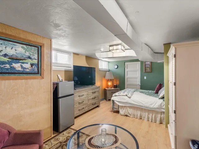 Finished basement space featuring wood-finish flooring, a wall-mounted television, a built-in window with horizontal blinds, and a paneled interior door