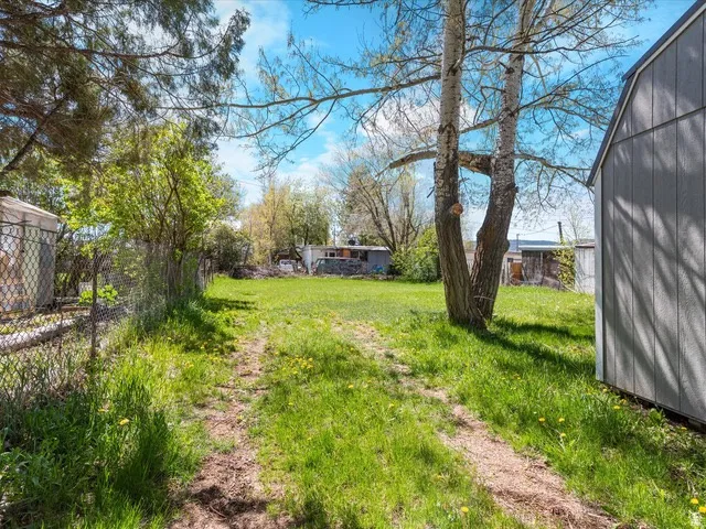 Spacious exterior featuring a grassy area, established trees, and a chain-link fence