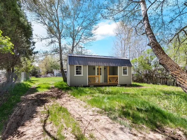 Detached outbuilding featuring a covered porch with natural wood railing, a gray corrugated metal roof, and light gray siding