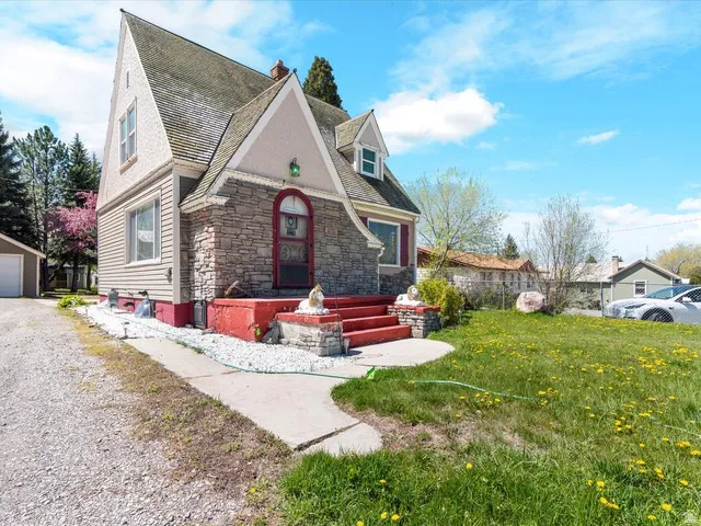 Exterior featuring stone and siding finishes, a prominent peaked roofline, a front porch with red-painted steps, and a gravel driveway