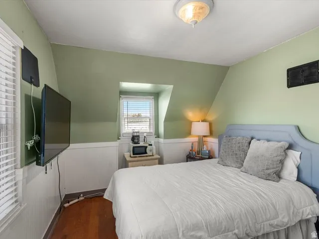 Bedroom featuring wood-finish flooring, white paneled wainscoting, and a window with blinds