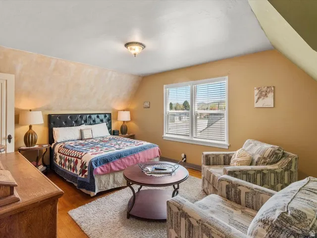 Sloped ceiling bedroom featuring hardwood flooring, a window with horizontal blinds, and a built-in light fixture