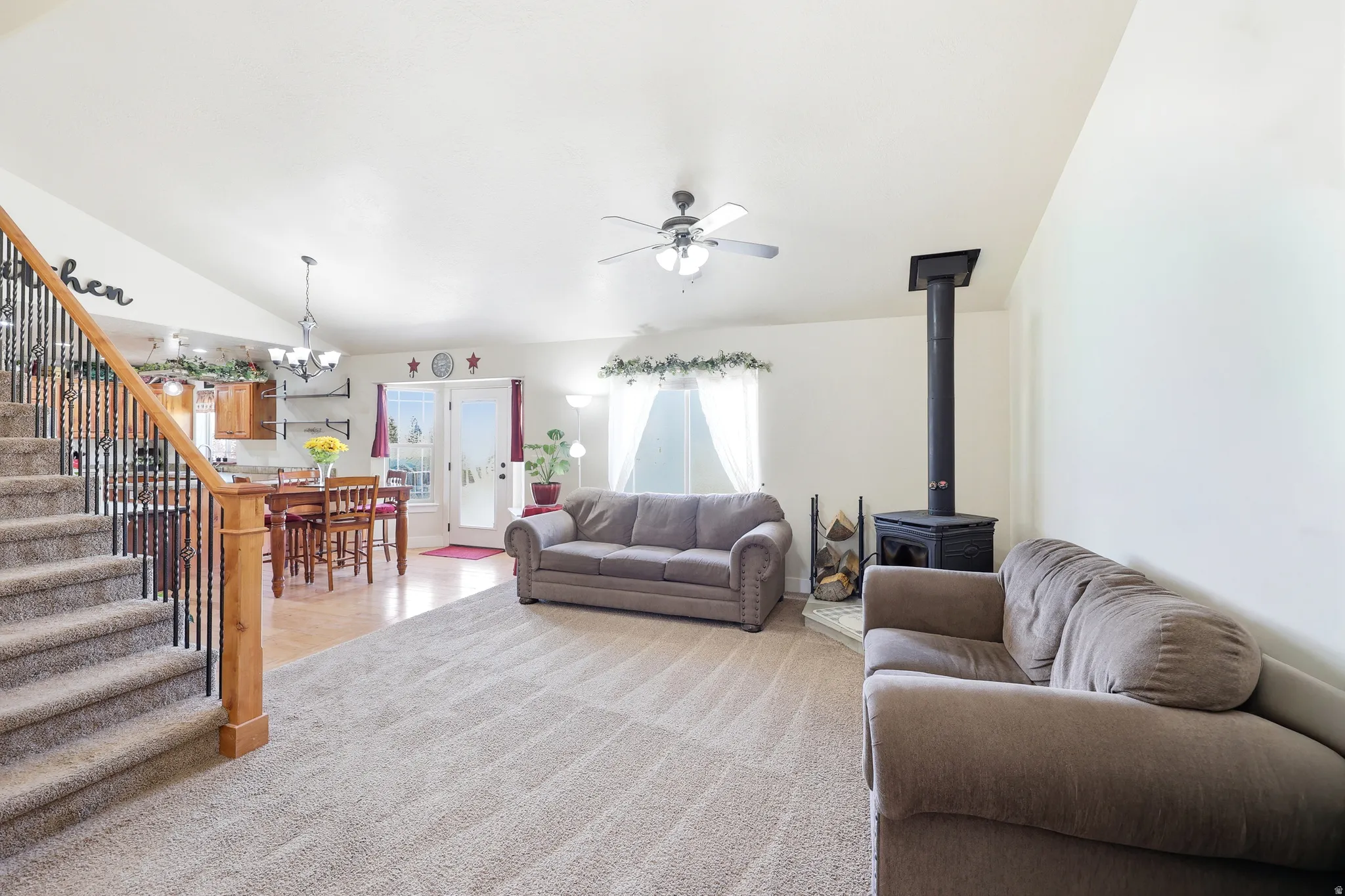 Open-concept living space featuring vaulted ceilings, a wood stove with a tile hearth, and carpeting