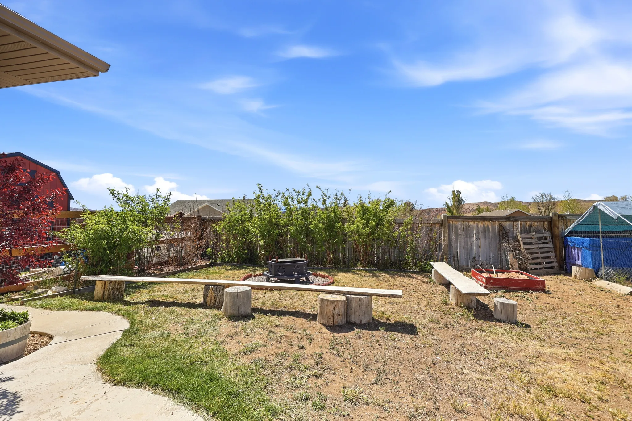 Expansive backyard featuring a fire pit, wood benches, and a concrete pathway