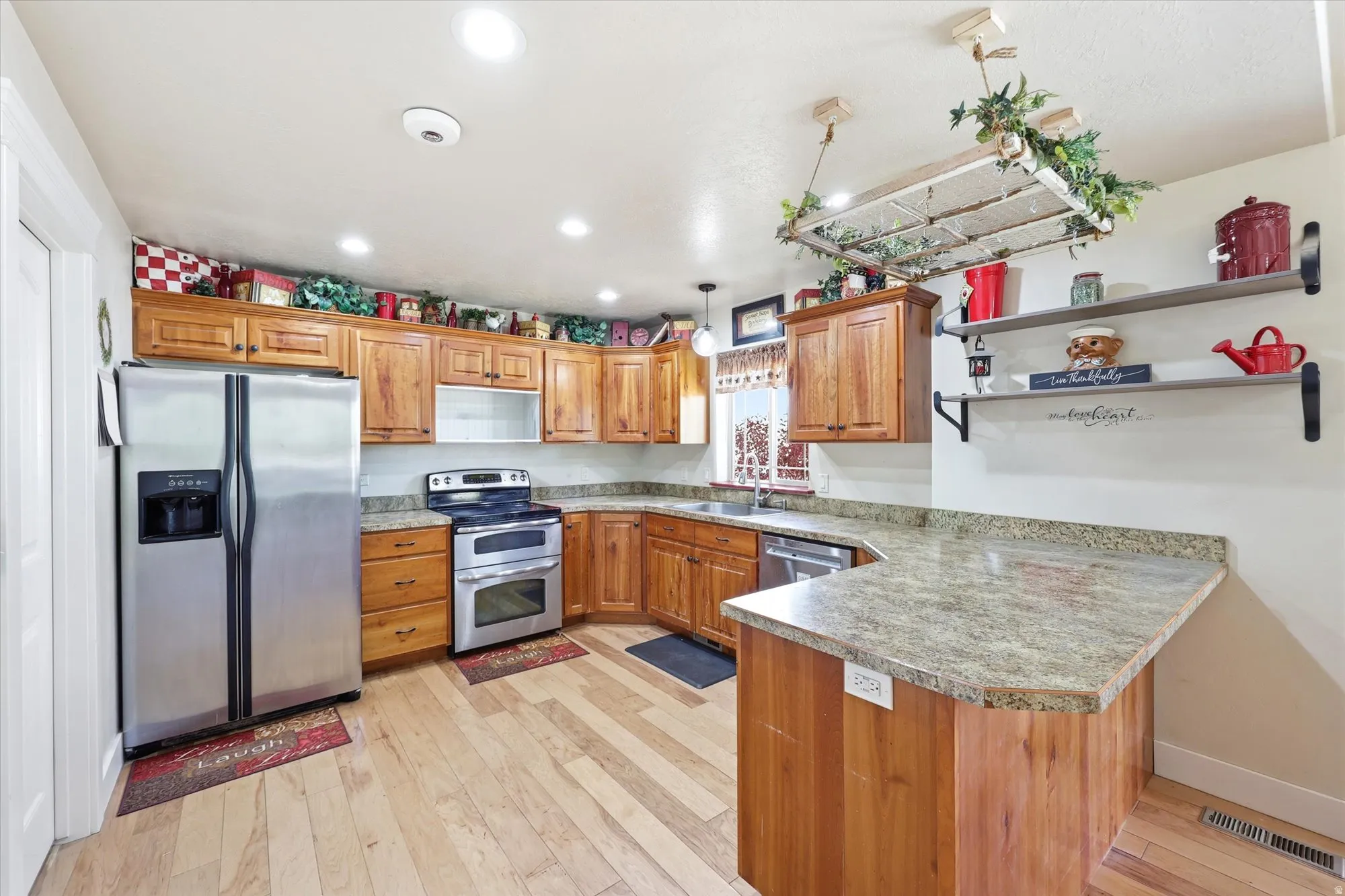 Kitchen featuring wood cabinetry, light-toned wood-finish flooring, recessed lighting, stainless steel appliances, and a peninsula with a stone-look countertop