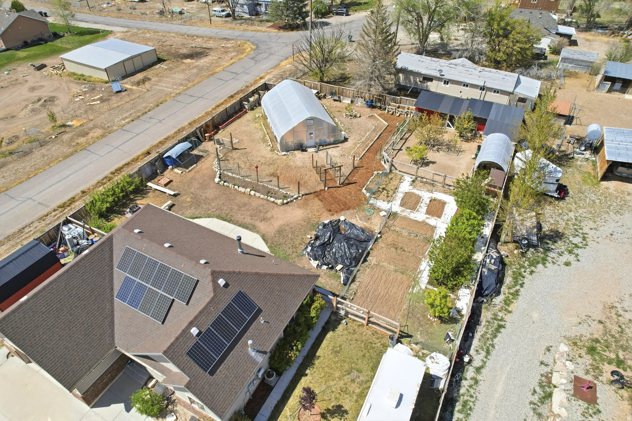 Rooftop solar panel arrays, hightunnel greenhouse, fenced garden areas, wood chip pathways, and a detached shed structure