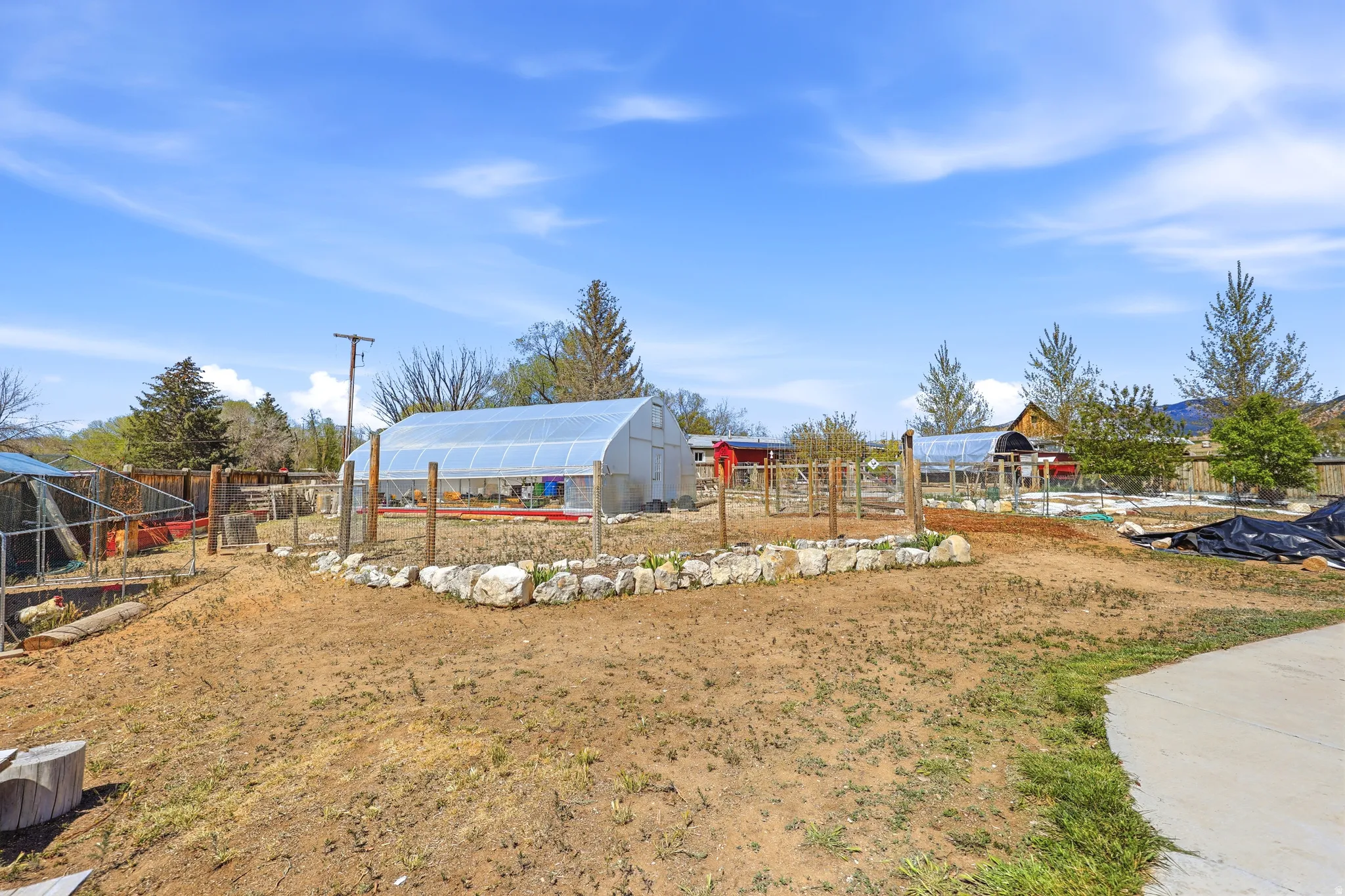 Expansive outdoor space featuring multiple greenhouses, fenced garden areas, and a paved pathway