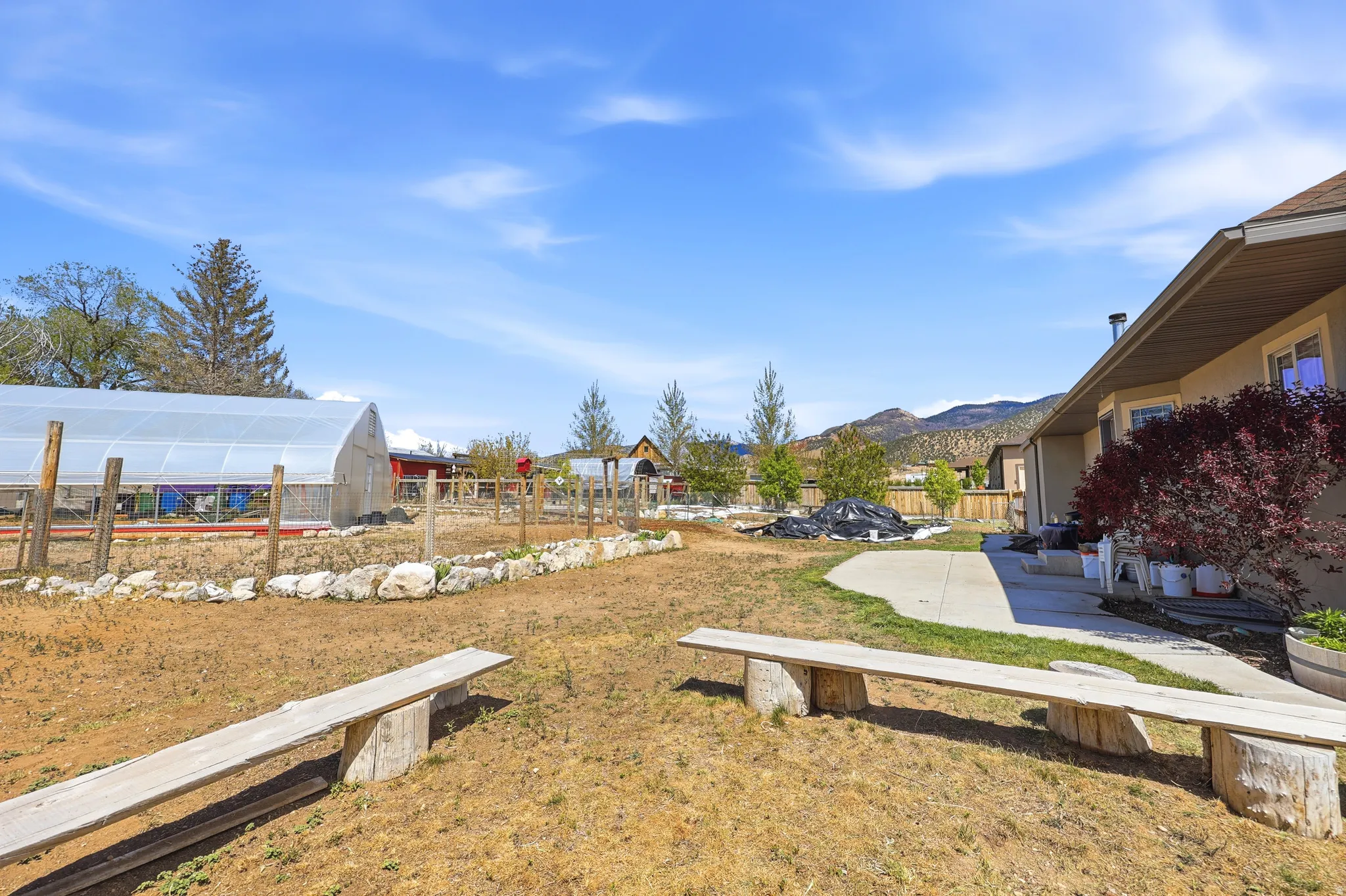Expansive backyard featuring a large greenhouse structure, a fenced garden area, and a paved patio