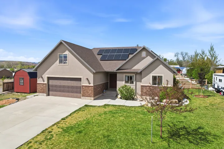 Contemporary home exterior featuring stucco and brick accents, an attached garage, a concrete driveway, rooftop solar panels, and a red detached shed