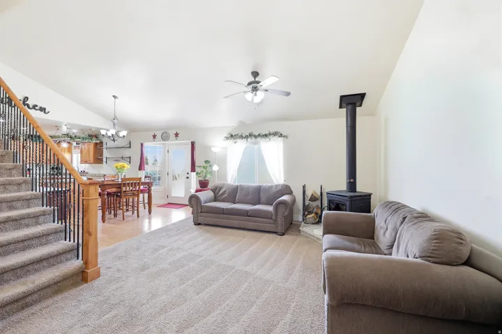 Open-concept living space featuring vaulted ceilings, a wood stove with a tile hearth, and carpeting