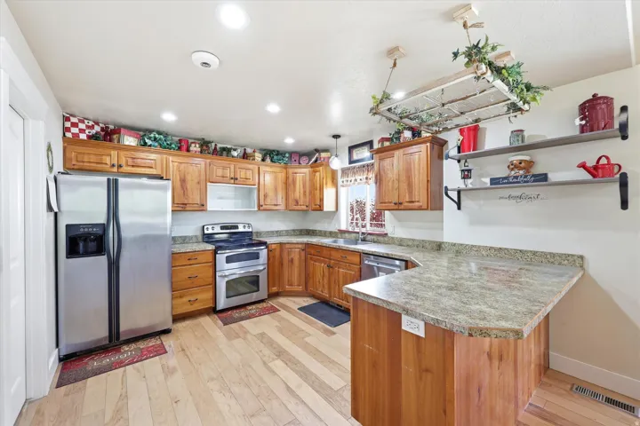Kitchen featuring wood cabinetry, light-toned wood-finish flooring, recessed lighting, stainless steel appliances, and a peninsula with a stone-look countertop