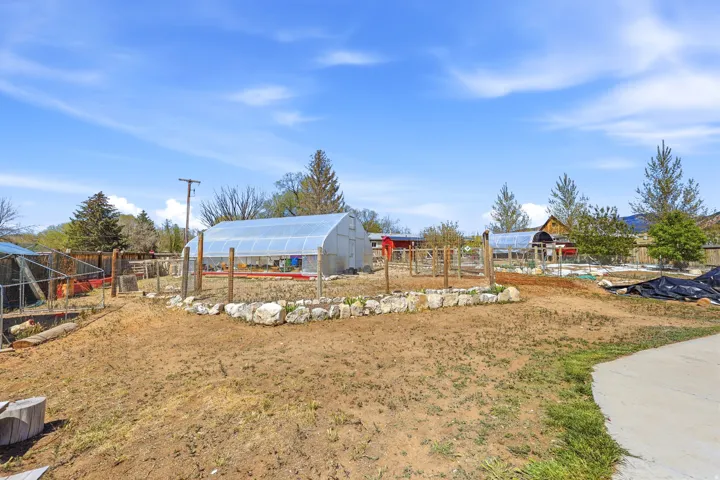 Expansive outdoor space featuring multiple greenhouses, fenced garden areas, and a paved pathway
