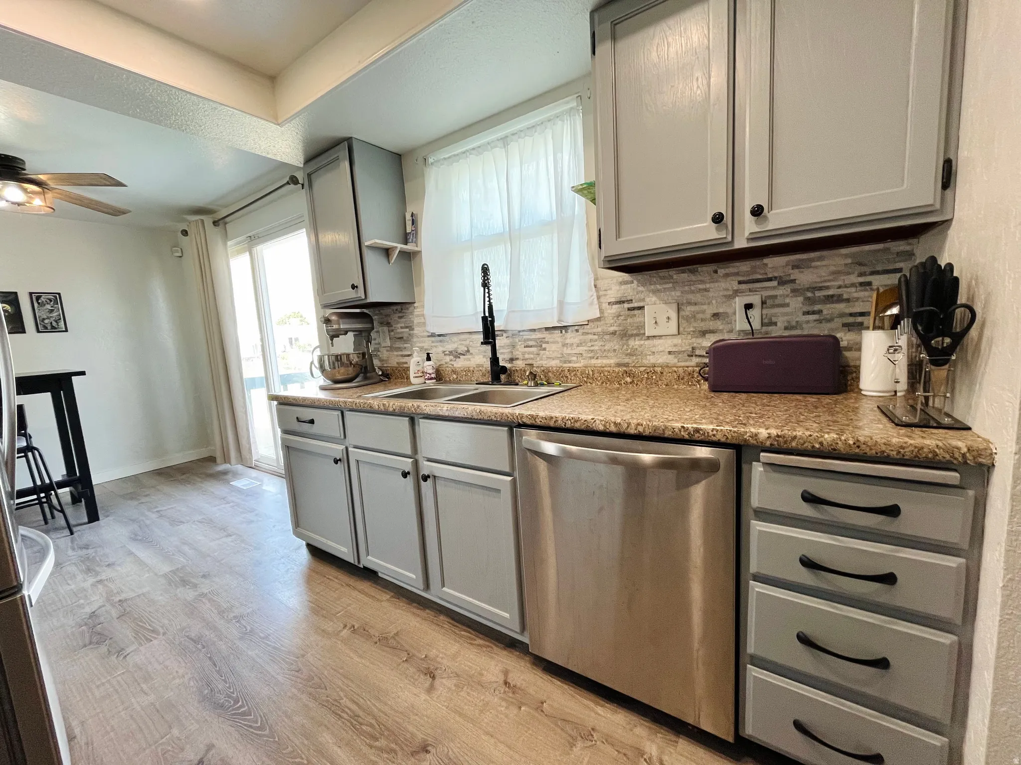Kitchen with gray cabinetry, LVP flooring, decorative backsplash and stainless-steel appliances, and recessed lighting.