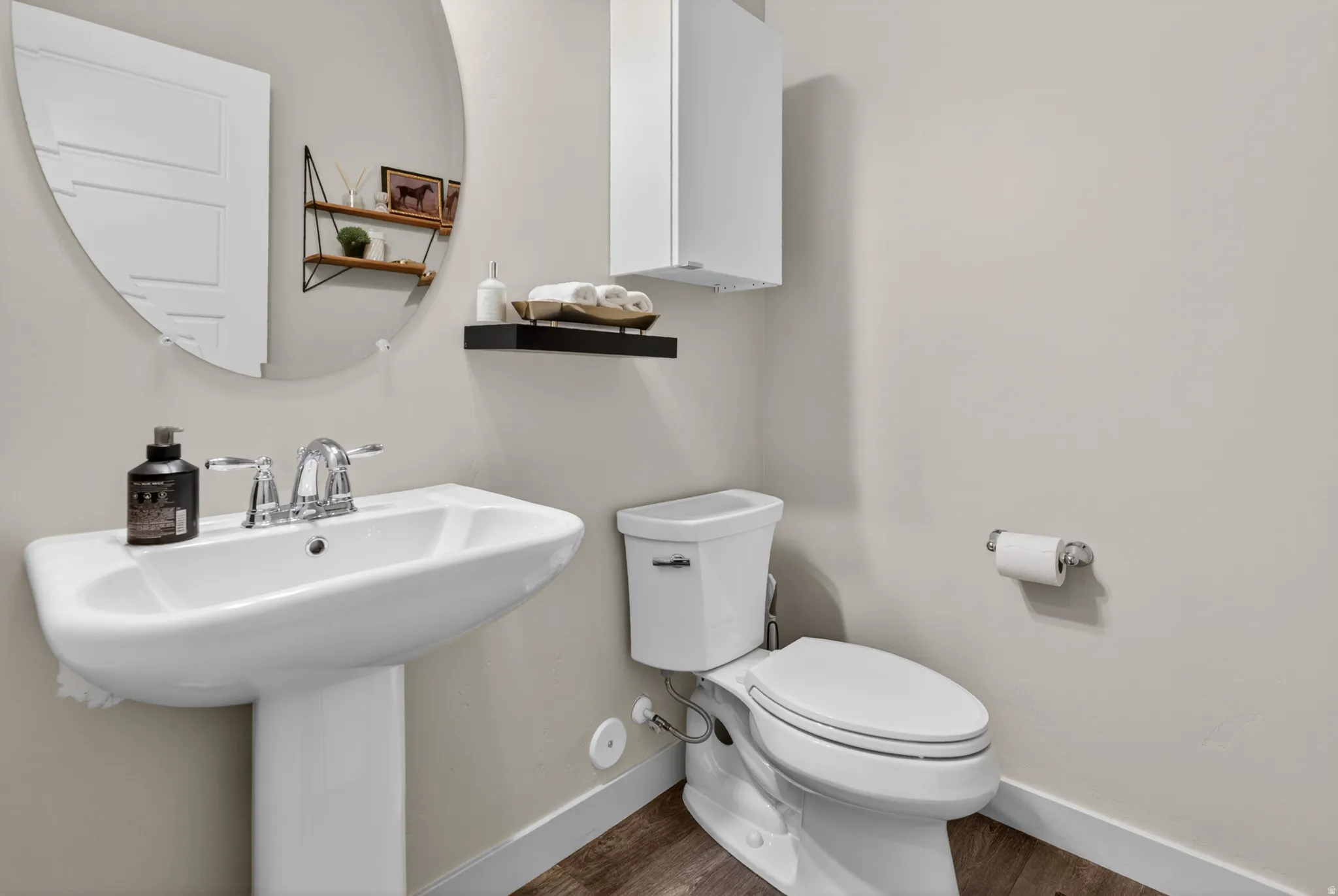 Pedestal sink with chrome fixtures and a circular wall mirror