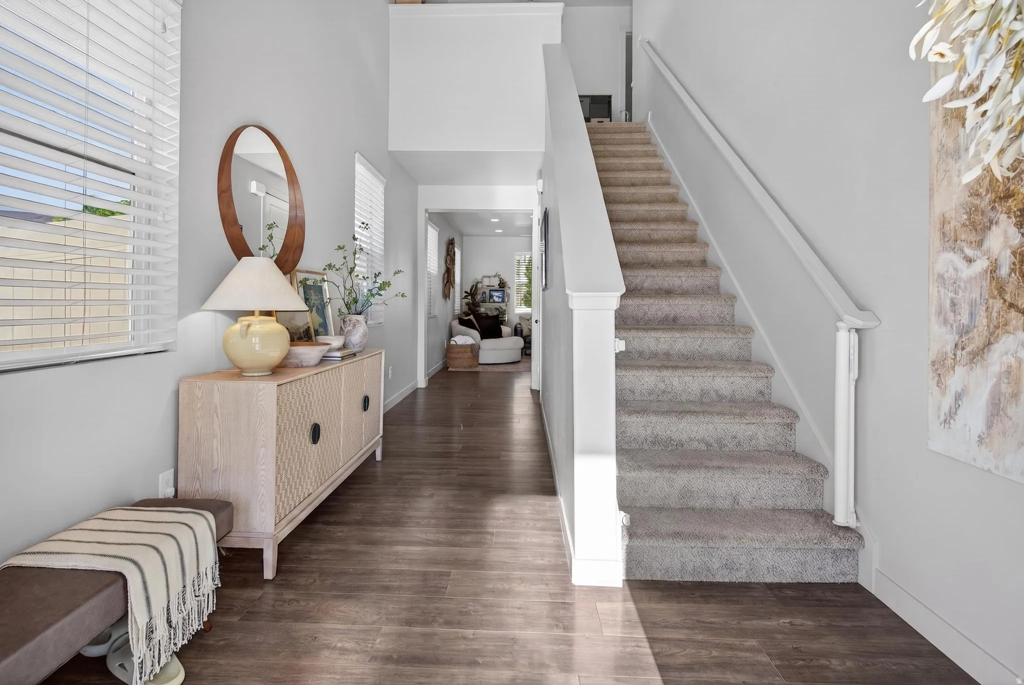 Entryway featuring wood-finish flooring, a carpeted staircase with white railings, and high ceilings