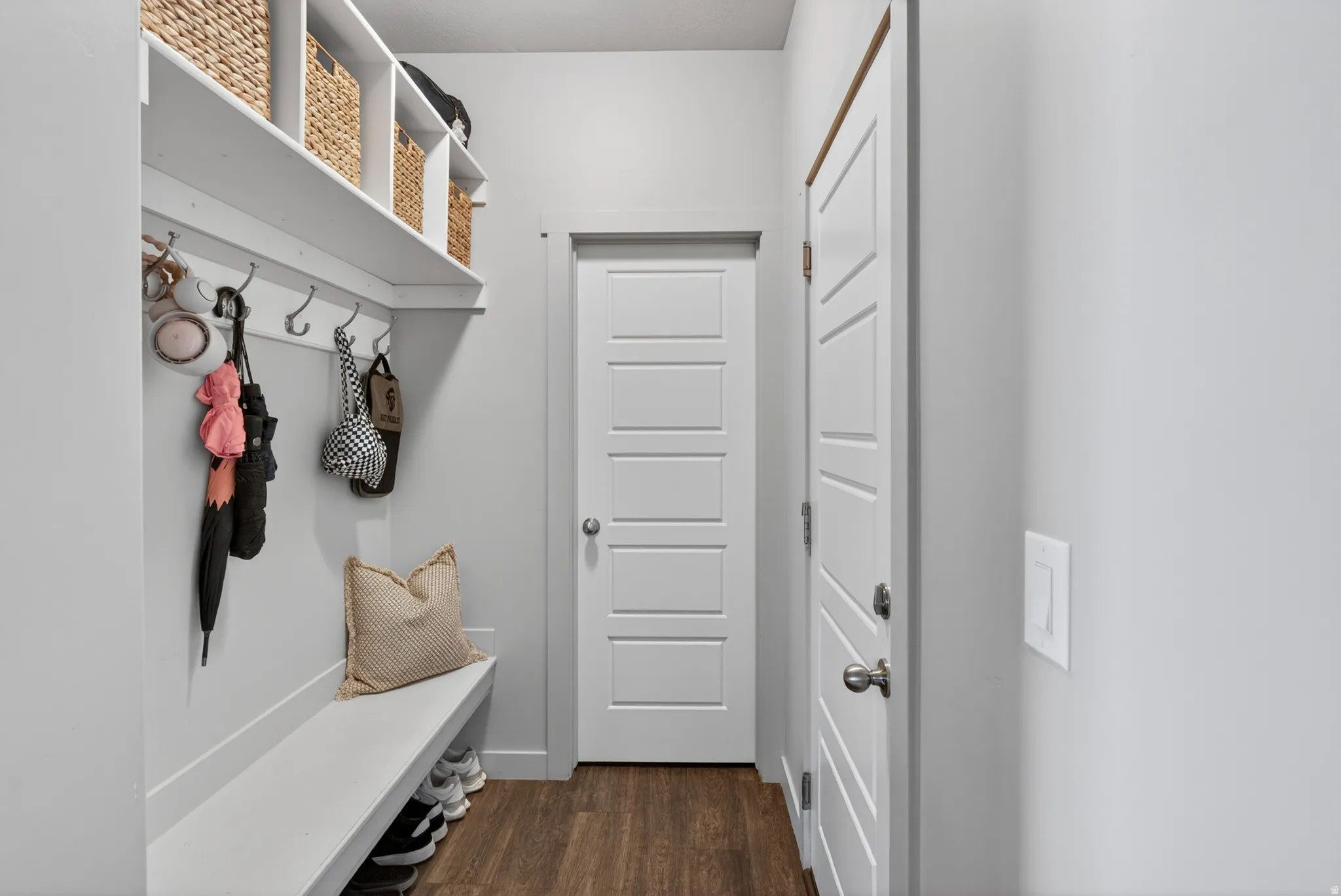 Entryway featuring wood-finish flooring, a built-in bench with integrated shelving, and a coat rack with multiple hooks