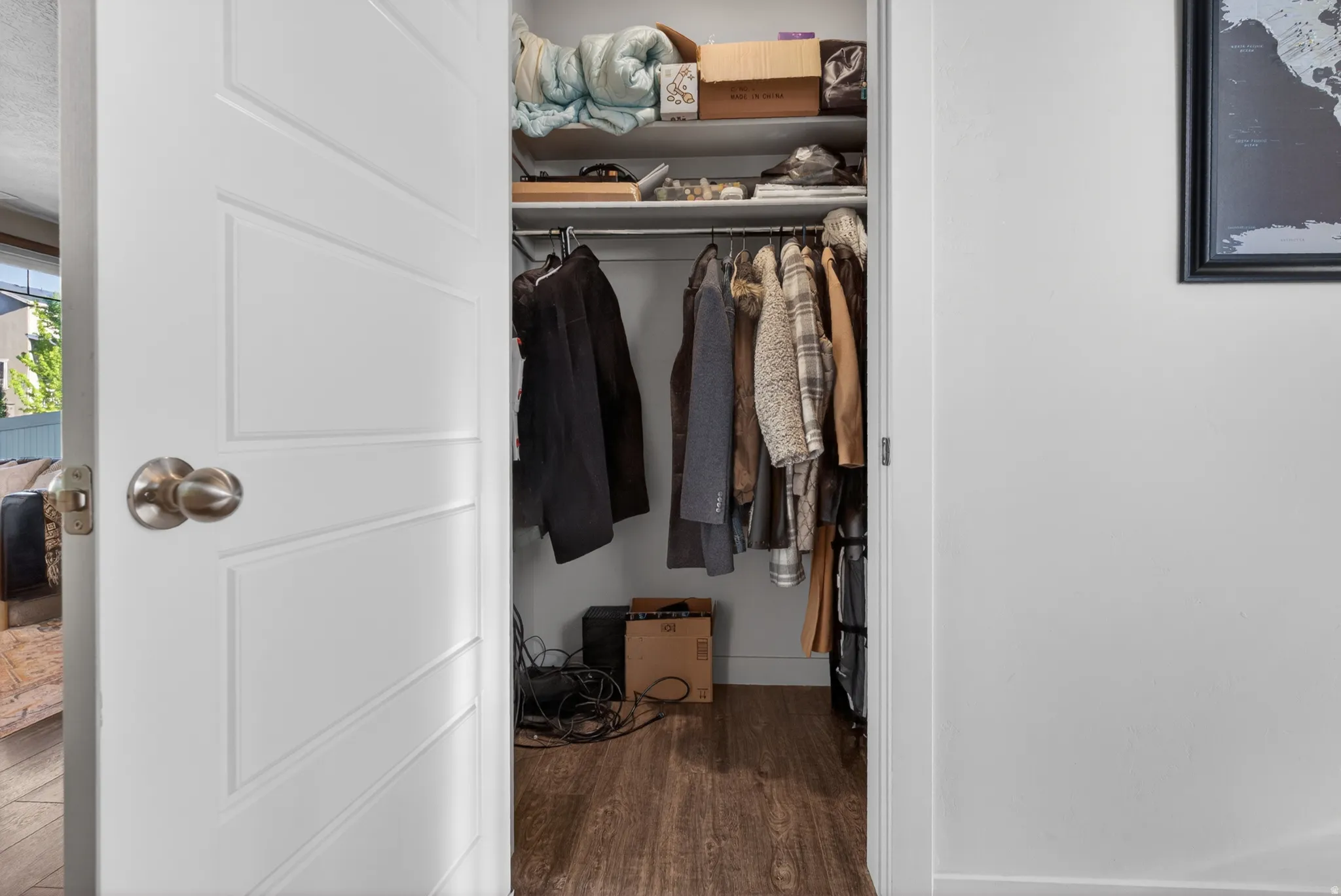 Interior closet featuring a white paneled door with brushed nickel hardware, wood-finish flooring, a clothing rod, and upper shelving
