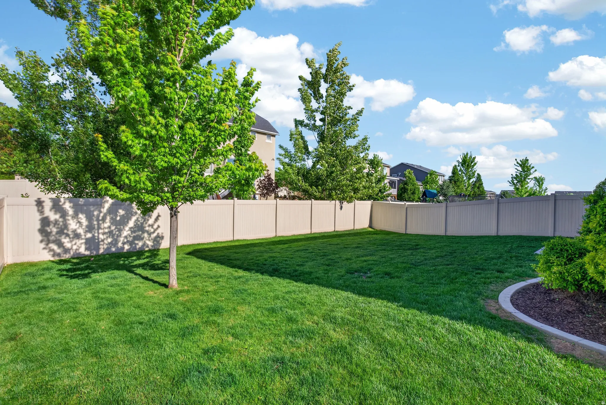 Expansive backyard featuring a lush green lawn, mature trees, and a full-perimeter privacy fence