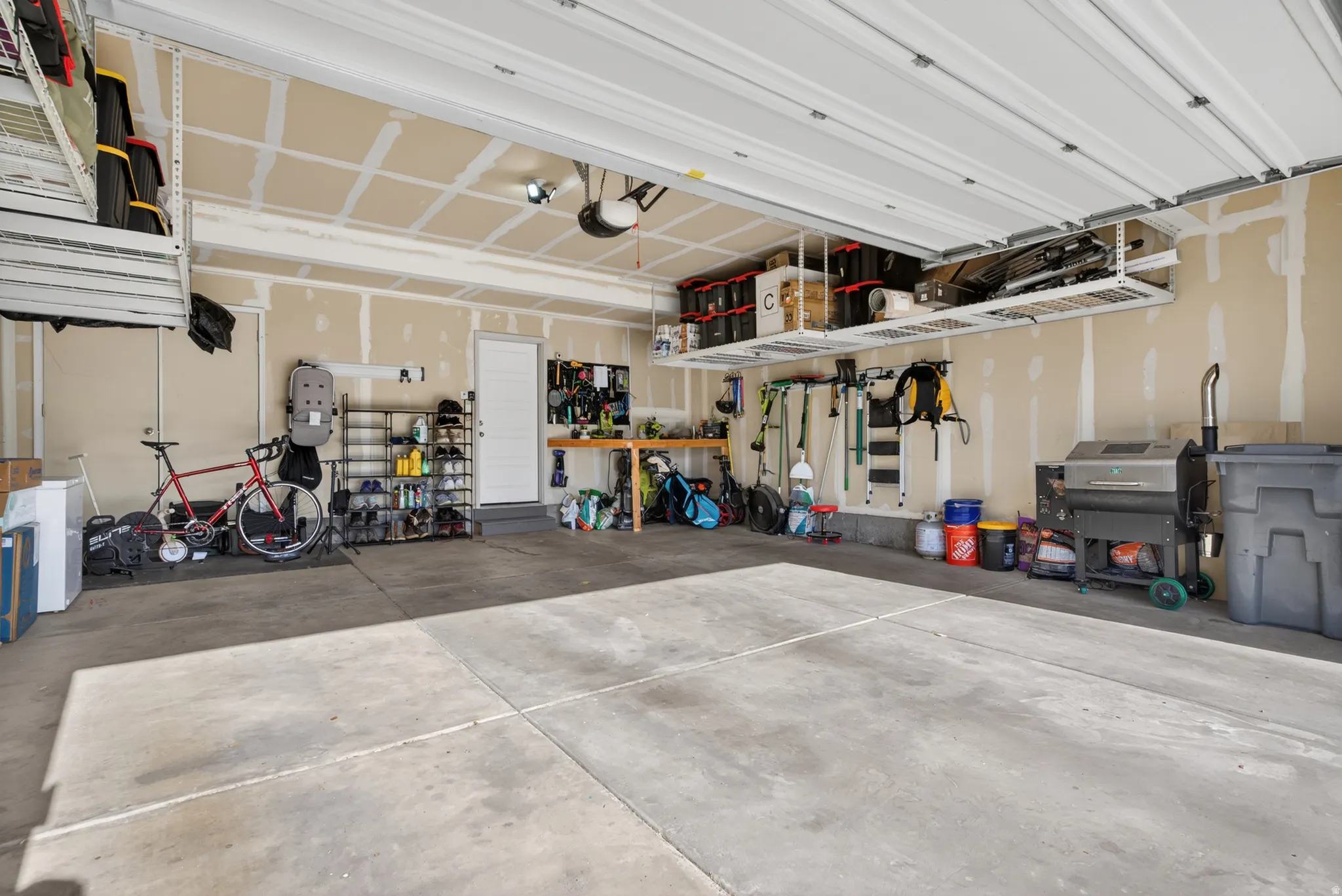 Spacious garage featuring a concrete floor, overhead storage racks, a side entry door, and exposed stud walls