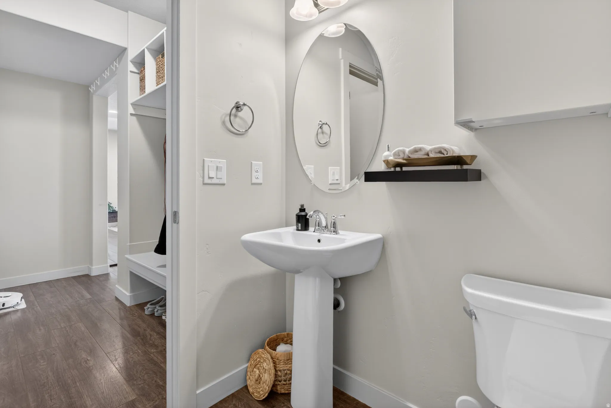 Pedestal sink with chrome faucet, oval mirror, and dark wood-finish flooring
