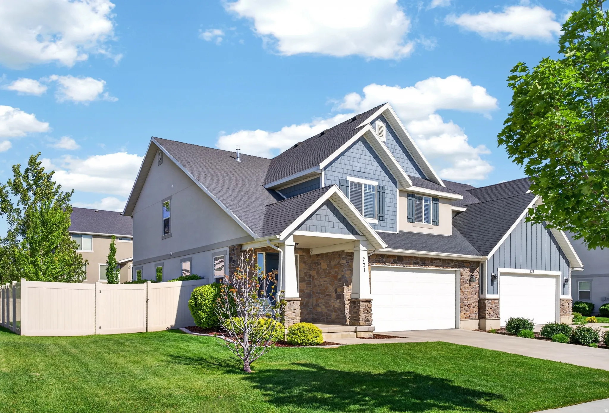 Multi-level residence featuring a gray asphalt shingle roof, mixed material facade with stone accents and blue siding, and a manicured green lawn