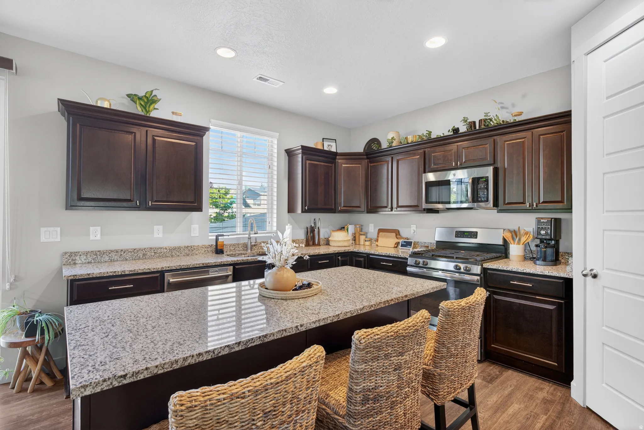 Spacious kitchen featuring dark wood cabinetry, light speckled countertops, stainless steel appliances, a center island with seating, and wood-finish flooring