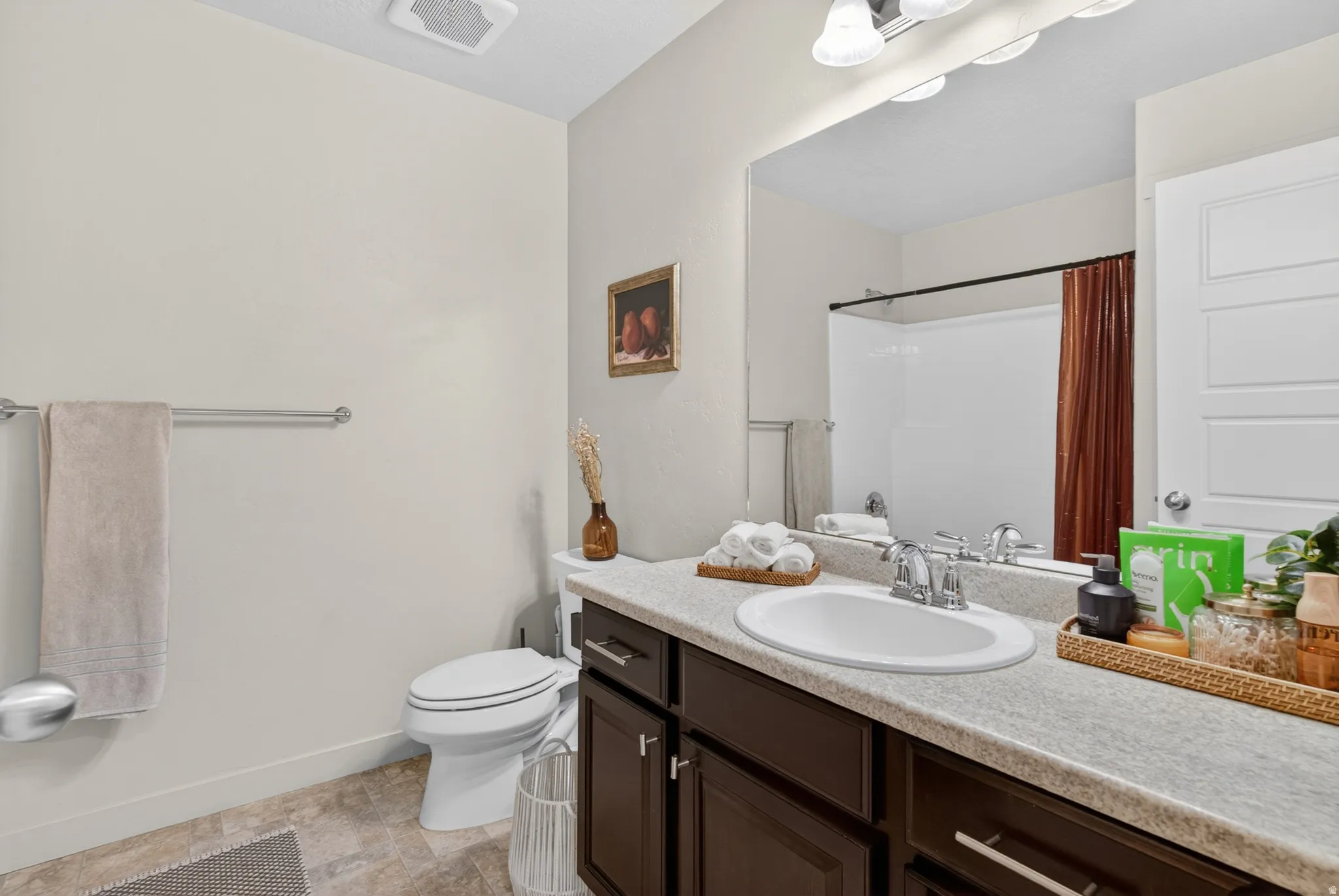 Bathroom featuring a single vanity with a solid surface countertop, an undermount sink, and dark wood cabinetry