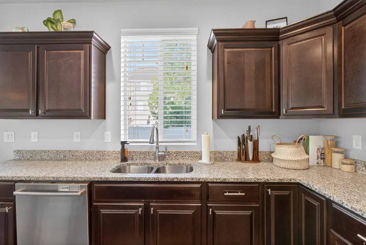 Kitchen featuring dark wood cabinetry, light speckled countertops, a stainless steel double basin sink, and a stainless steel dishwasher
