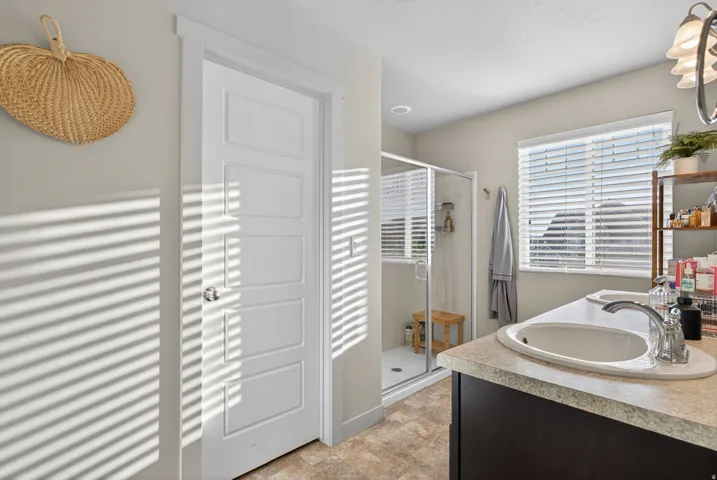 Bathroom featuring a dual vanity with undermount sinks, a shower enclosure with glass doors, a single window with blinds, and recessed lighting