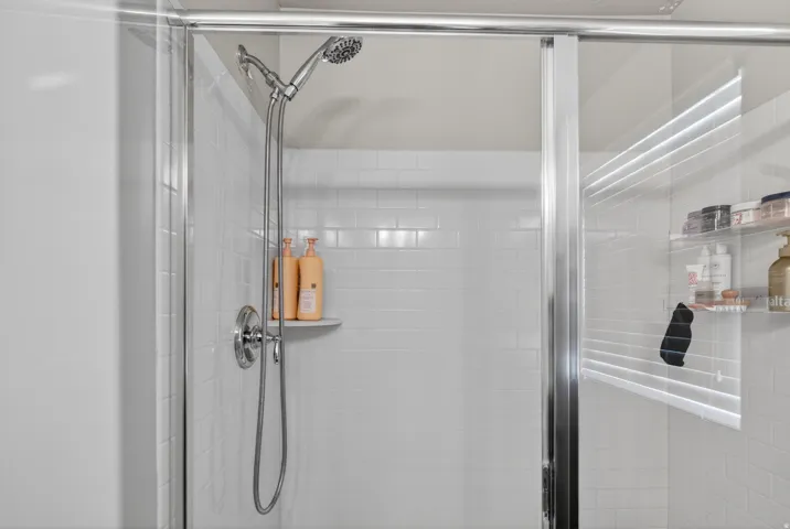 Shower enclosure featuring a chrome-finish sliding glass door, subway tile surround, recessed shelf, and a multi-function showerhead with a handheld sprayer
