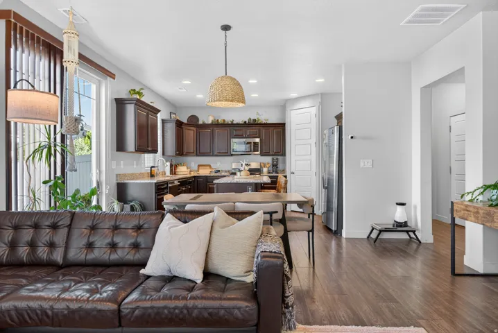 Open-concept living space featuring wood-finish flooring throughout, a kitchen with dark wood cabinetry and light-colored countertops, and a dining area with a modern woven pendant light