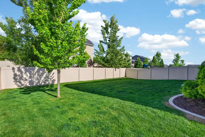 Expansive backyard featuring a lush green lawn, mature trees, and a full-perimeter privacy fence