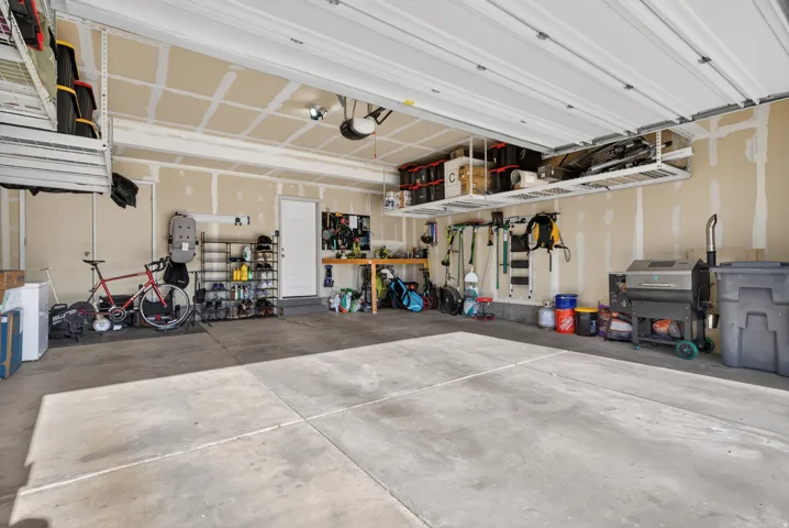 Spacious garage featuring a concrete floor, overhead storage racks, a side entry door, and exposed stud walls