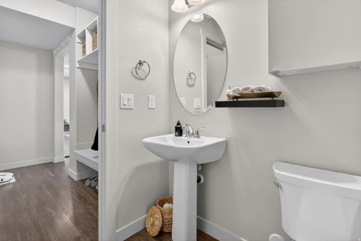 Pedestal sink with chrome faucet, oval mirror, and dark wood-finish flooring