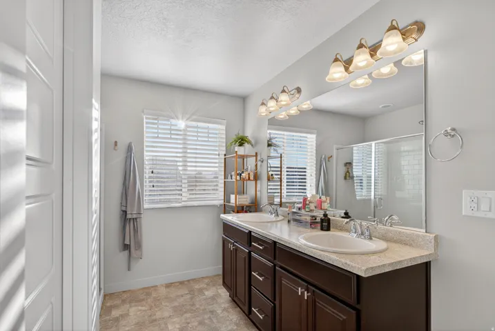 Double vanity with integrated sinks, ample storage cabinetry, and a large mirror with sconce lighting